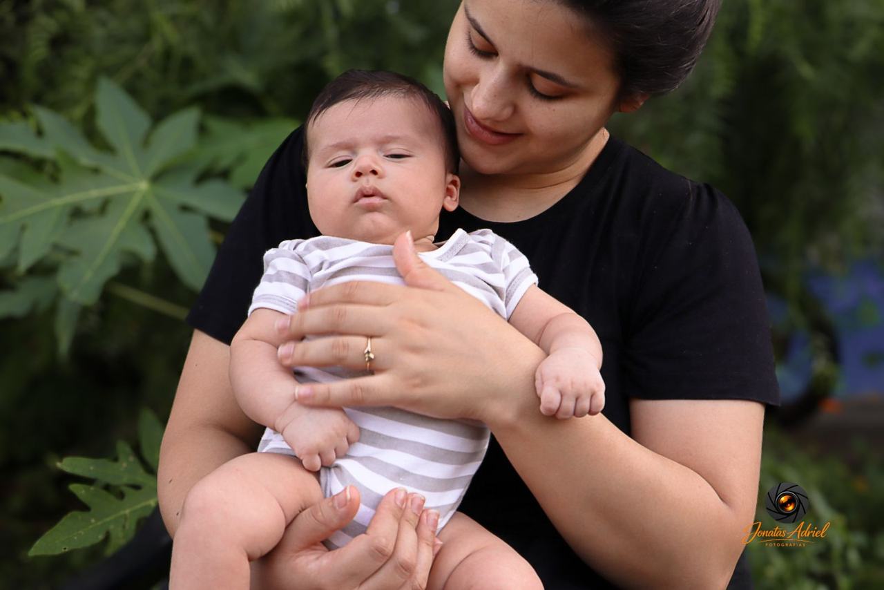 Mãe segurando bebê no colo entre plantas