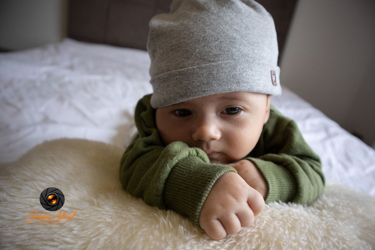 Bebê de touca e casaco verde na cama