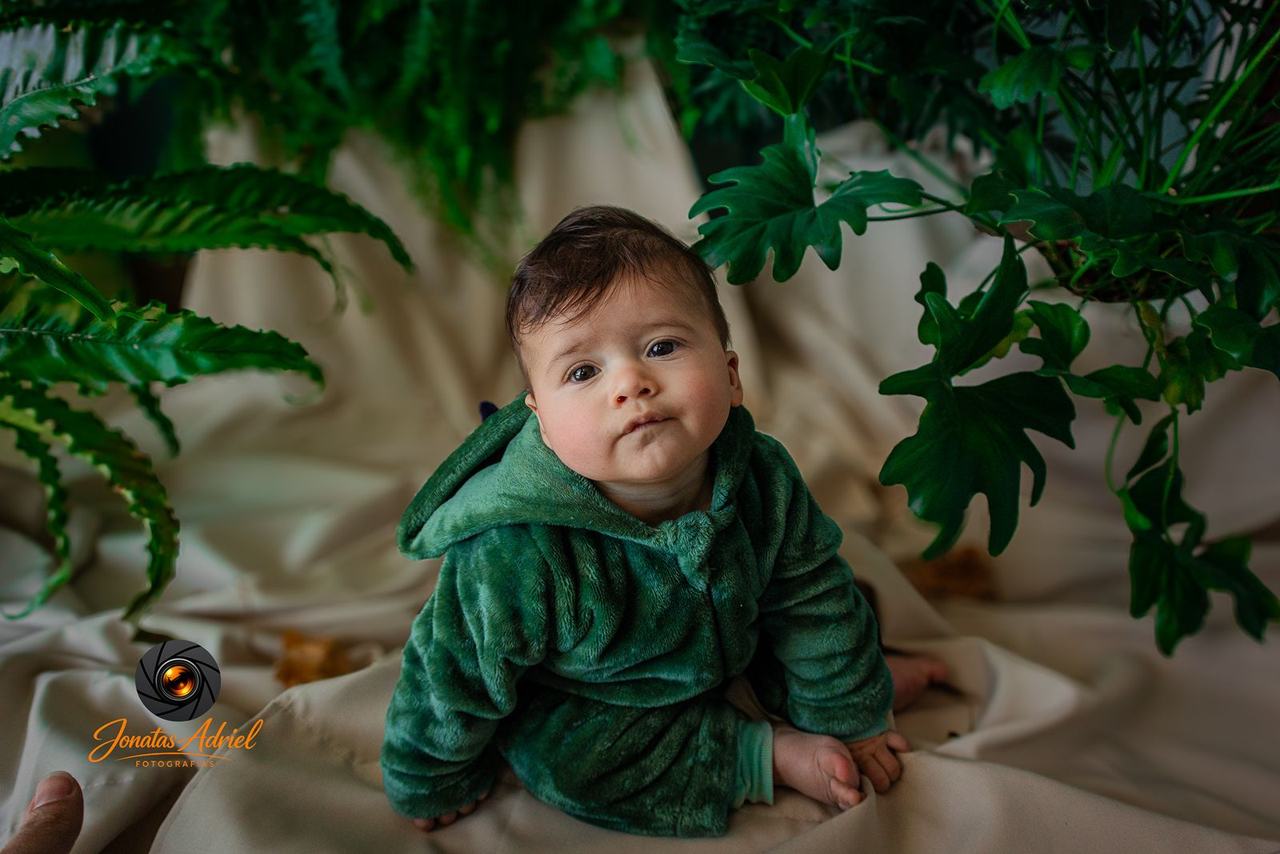 Bebê fantasiado de dinossauro entre plantas, de perto