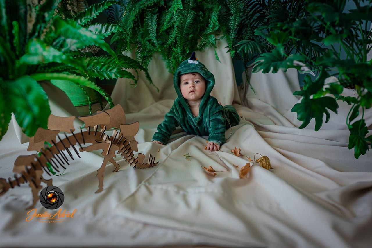 Bebê fantasiado de dinossauro ao lado de esqueleto de brinquedo