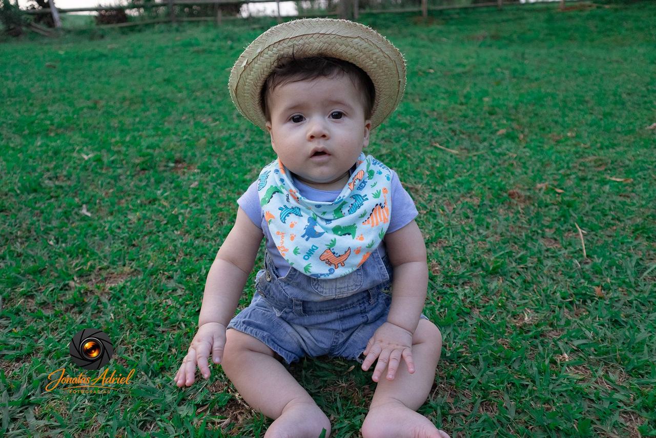 Bebê com chapéu de palha sentado na grama